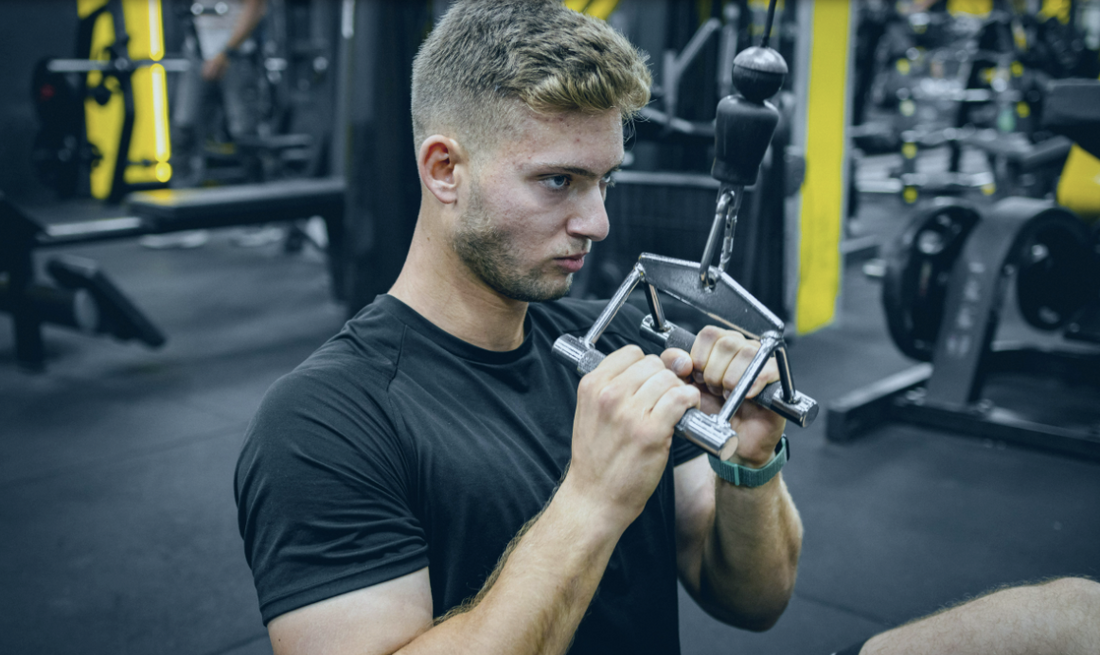 Athlète en salle de sport réalisant un exercice de préparation musculaire avant l'entraînement, échauffement des bras et des épaules pour réduire le risque de blessure et améliorer la performance.