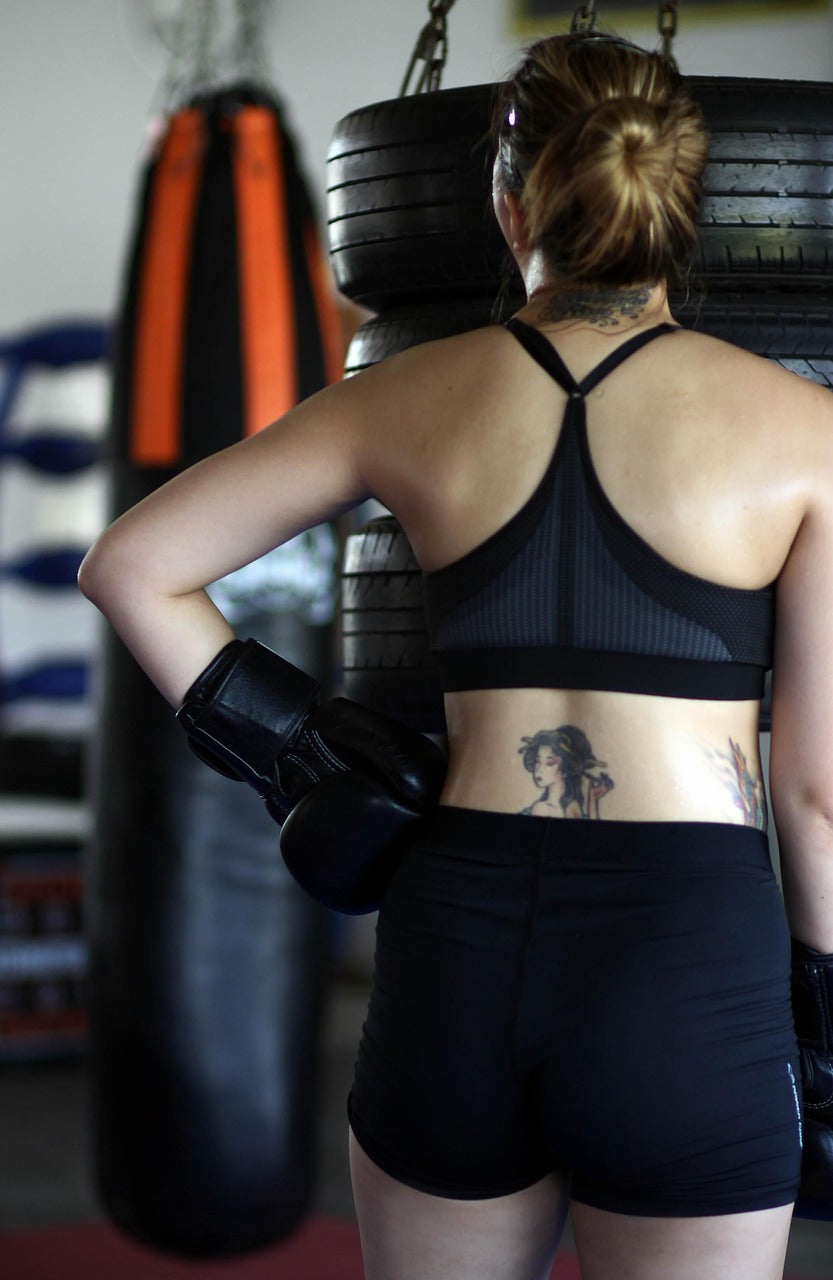 Boxeuse de dos en salle de boxe préparant ses épaules avant l’entraînement.