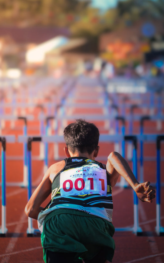 Un jeune coureur avec un dossard numéroté se prépare pour une course de haies sur une piste ensoleillée.